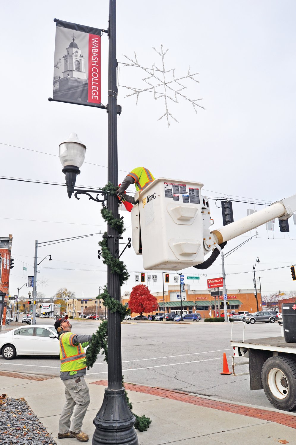 Chris Hartman (on the ground) and Nathan Whitlow of the Crawfordsville Street Department wrap garland around a light pole along East Market Street Tuesday.